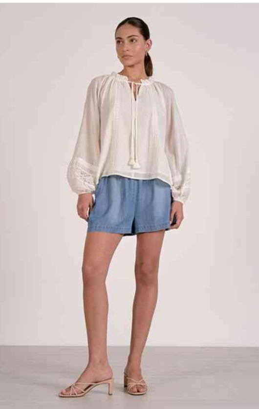 Woman wearing a white blouse and denim shorts on a plain background