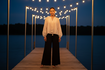 Ivory colored flowy top with billowing long sleeves on a wiman standing in a dock. 