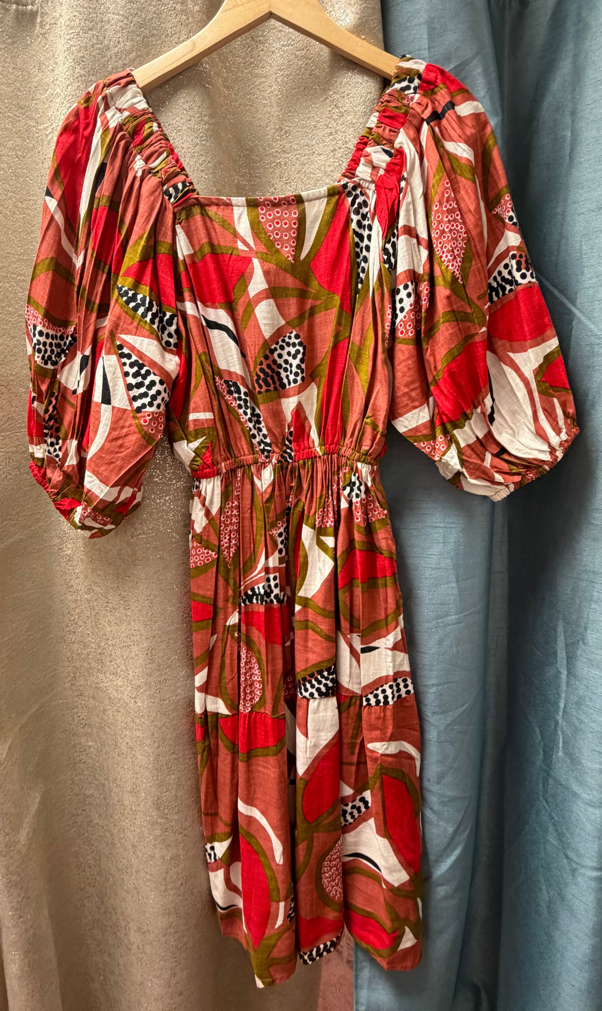 Colorful Dragonfruit Peasant Dress on a hanger against a curtain background