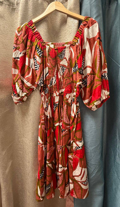 Dragonfruit Peasant Dress hanging on a rack with beige and blue curtains in the background