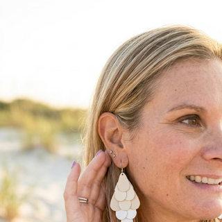 Smiling woman at the beach wearing matte silver Cascade Teardrop Dangle Earrings, layered teardrop petals in a cascading dangle
