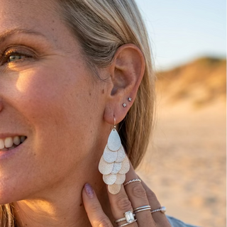 Close-up of matte silver Cascade Teardrop Dangle Earrings worn at the beach, showing the layered teardrop design