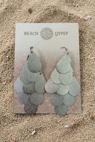 Matte silver Cascade Teardrop Dangle Earrings with layered teardrop petals on a Beach Gypsy earring card, resting on beach sand
