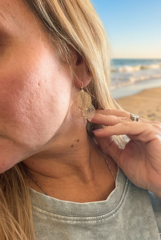 Woman wearing Gold-Tone Layered Filigree Leaf Dangle Earrings with a gray sweatshirt, ocean in the background