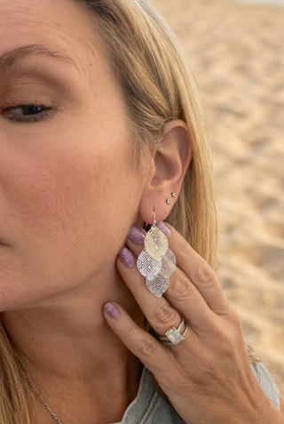 Woman at the beach wearing Silver-Tone Filigree Layered Leaf Dangle Earrings, hand raised near her ear