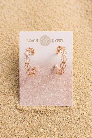 Gold-Tone Openwork Filigree Hoop Earrings with a wavy openwork design on a Beach Gypsy earring card, resting in beach sand