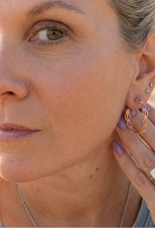 Woman wearing Gold-Tone Openwork Filigree Hoop Earrings, hand raised near her ear to show the wavy filigree hoop
