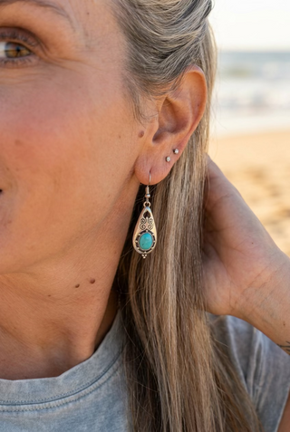 Woman at the beach wearing Turquoise-Color Scrollwork Teardrop Earrings, hand resting at her neck