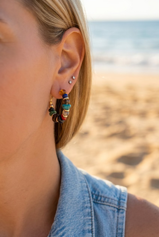 Woman at the beach wearing multicolor beaded hoop earrings with a denim top