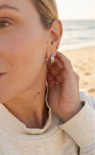 Woman at the beach wearing Silver-Tone Ridged Hoop Earrings with a cream sweater, hand near her ear