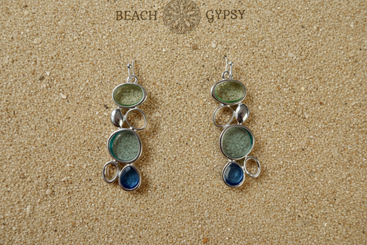 Pair of silver and green earrings on a sandy background with 'Beach Gypsy' branding.
