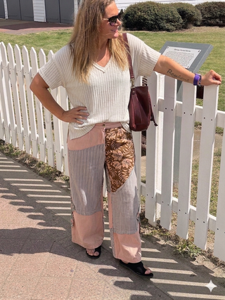 Woman standing by a white picket fence, wearing a white top and patterned pants.