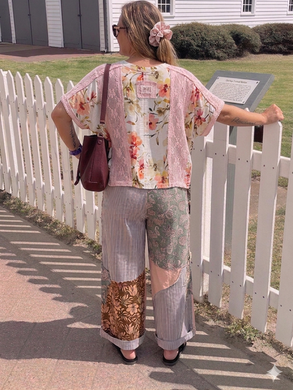 Woman in floral top and patchwork pants standing near a white picket fence.