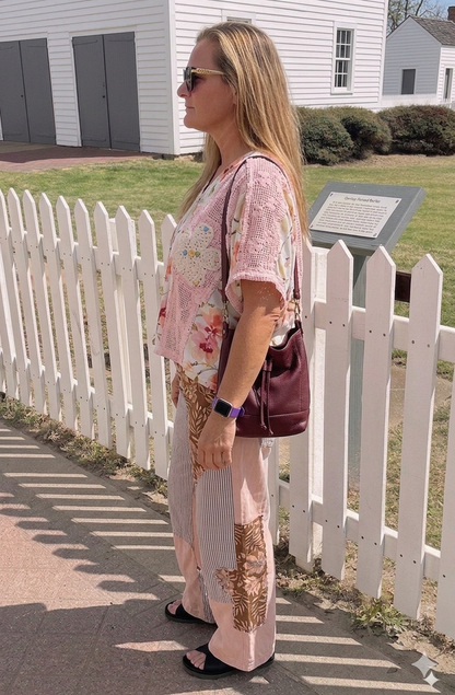 Woman in a floral dress standing near a white picket fence with a building in the background