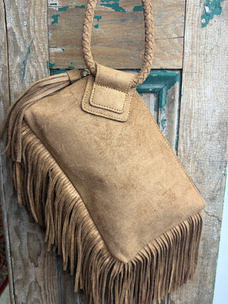 Tan sueded fringe wristlet bag with braided ring handle and front flap, hanging on a rustic wood door