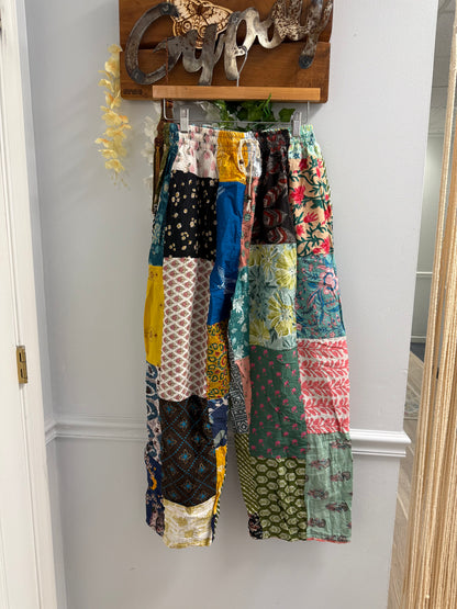 Colorful patchwork pants hanging on a rack against a white wall.