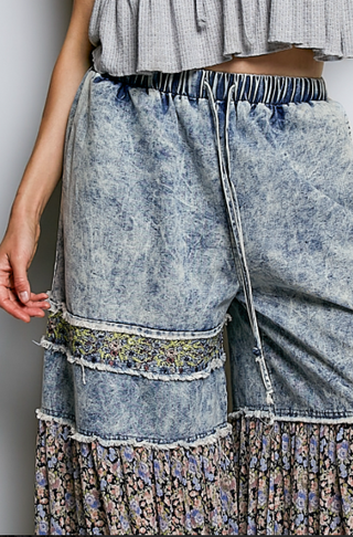 Person wearing a denim skirt with floral patterned hem on a plain background
