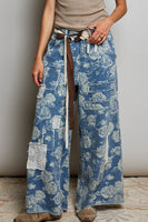 Person wearing blue floral-patterned pants with a brown belt against a neutral background