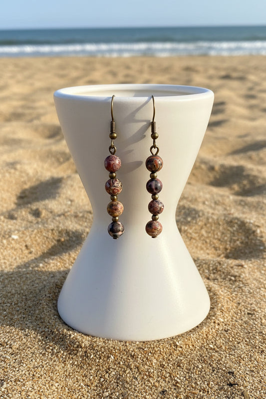 Pair of beaded earrings on a pedestal on sandy beach background

