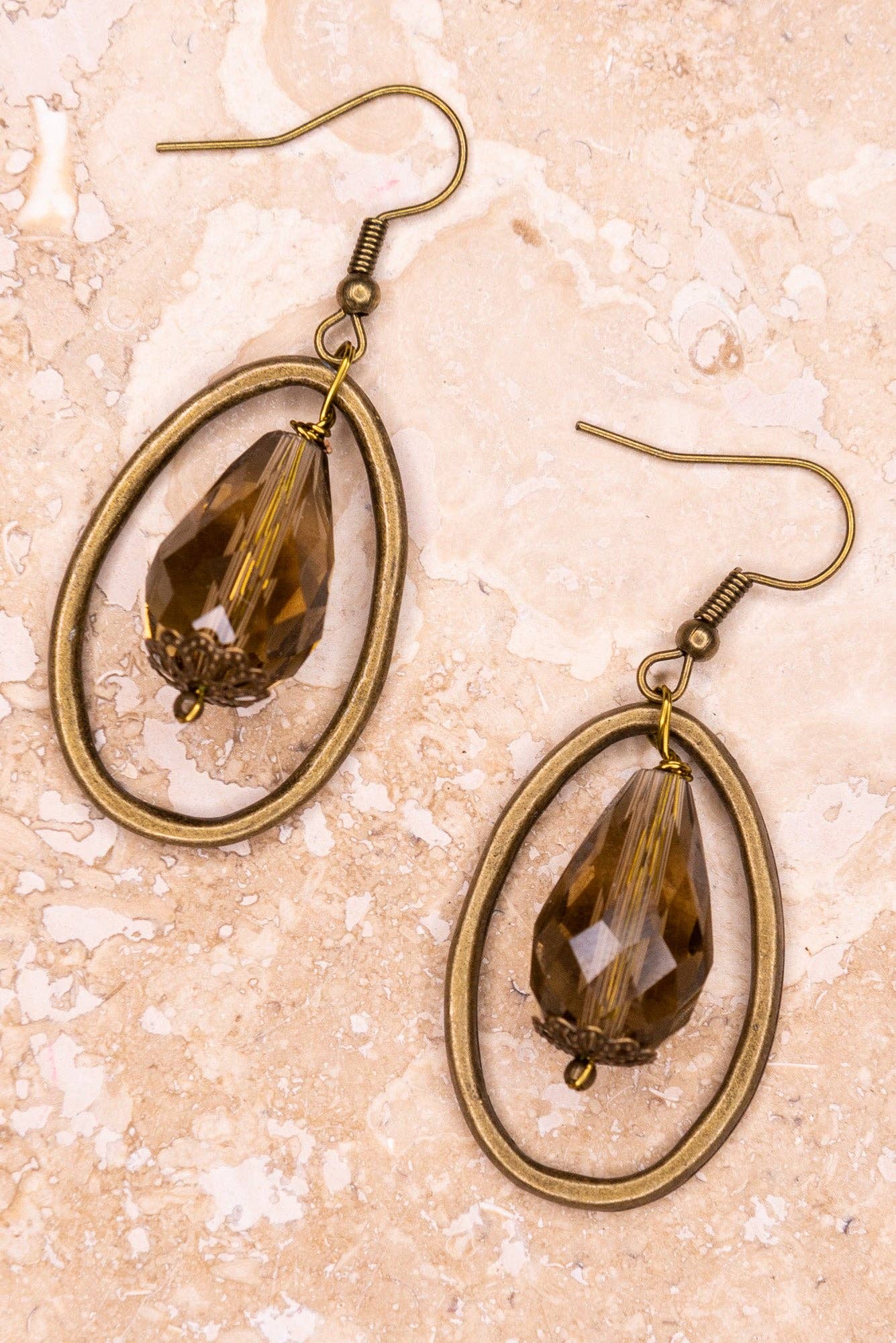 Pair of earrings with smoky glass stones and bronze frames on a beige textured background