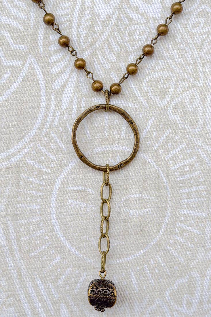 Bronze necklace with circular pendant and beads on a textured beige background