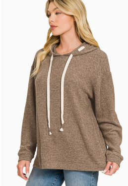 A woman wearing a brown heathered pullover hoodie with cream-colored drawstrings, paired with blue jeans, shown against a plain white background.