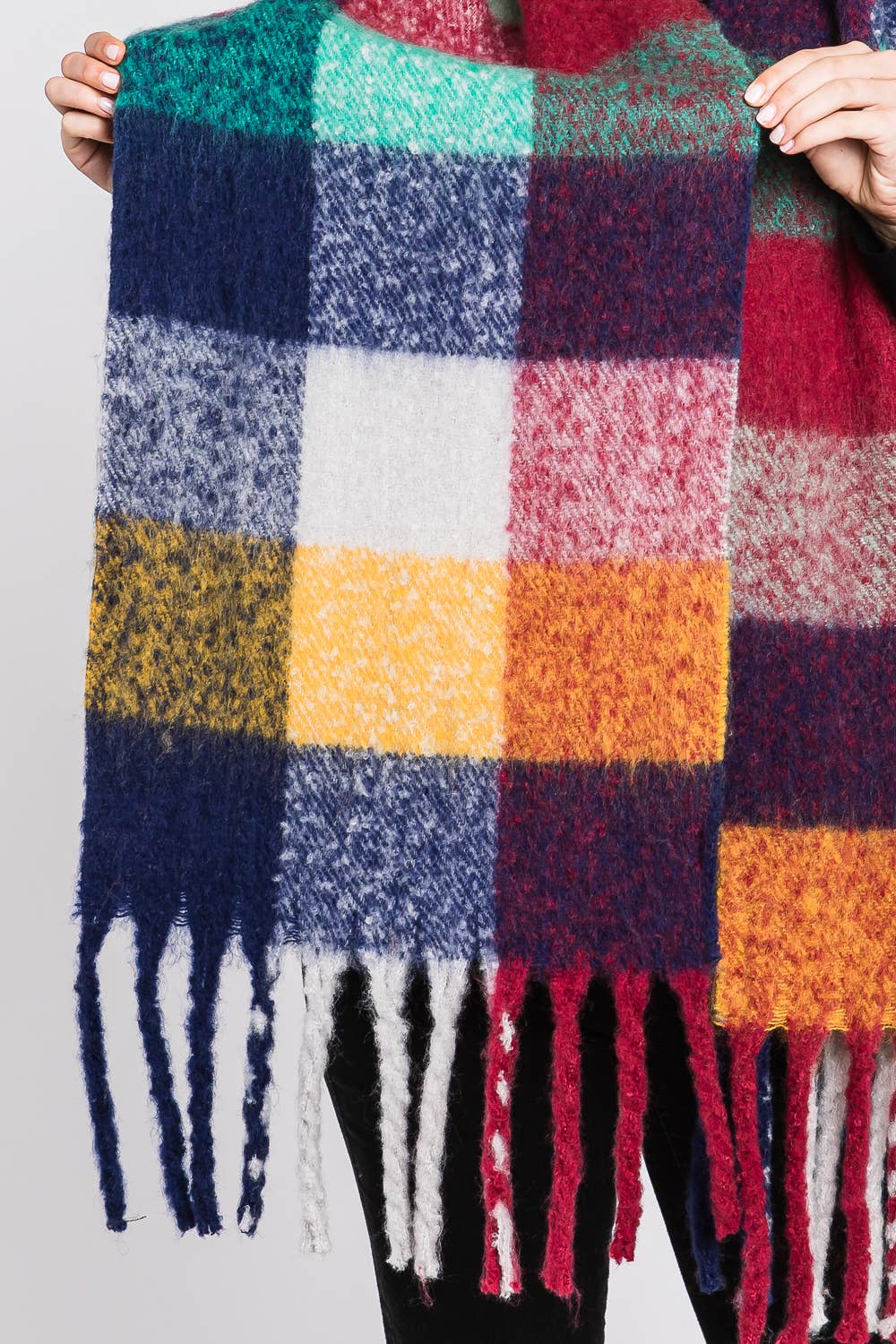 Multicolored checkered scarf with fringes held by a person against a neutral background