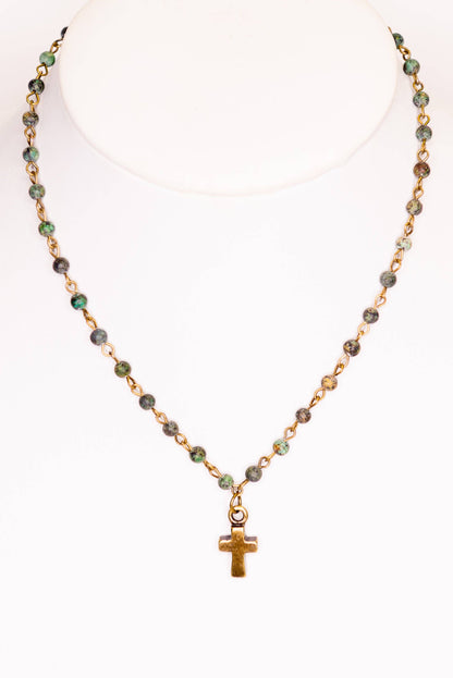 Necklace with green beads and a gold cross pendant on a white background