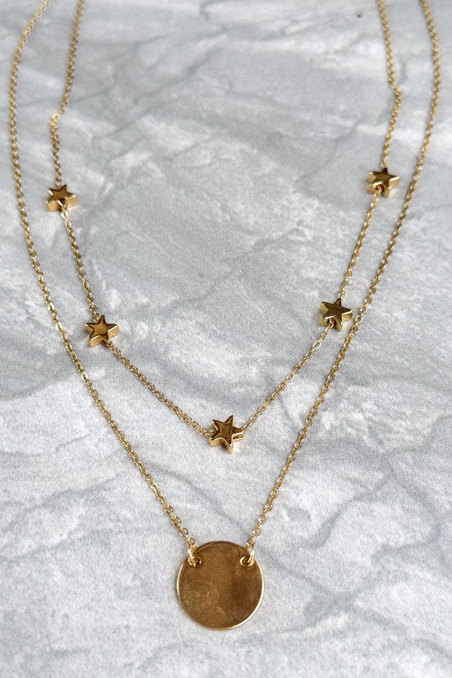 Two gold necklaces with star pendants on a marble surface