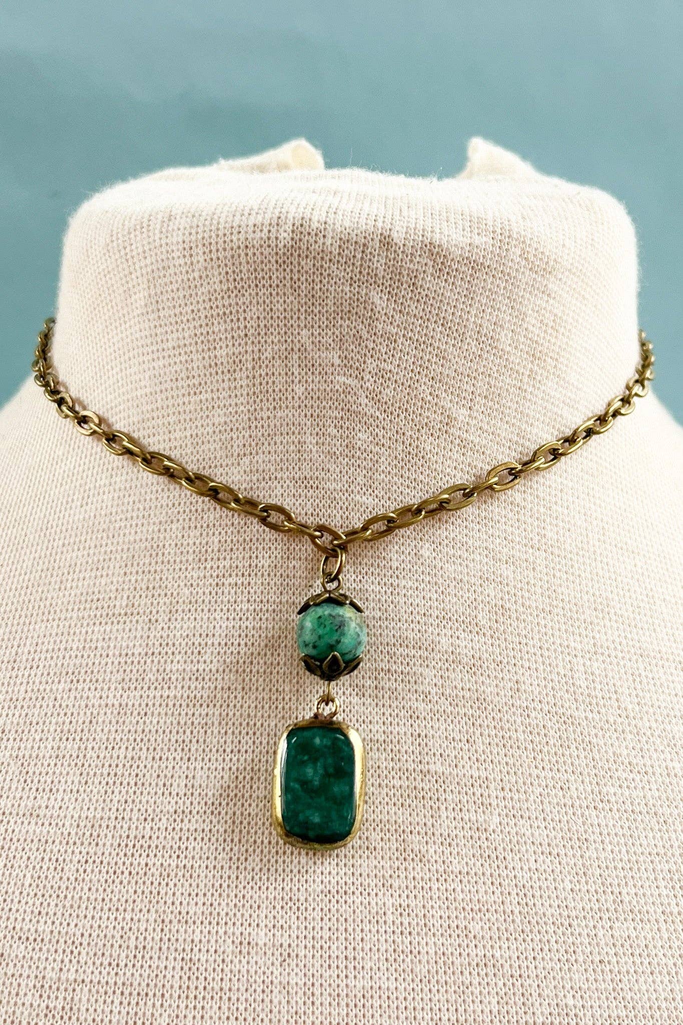Necklace with green pendant on a mannequin bust against a light blue background