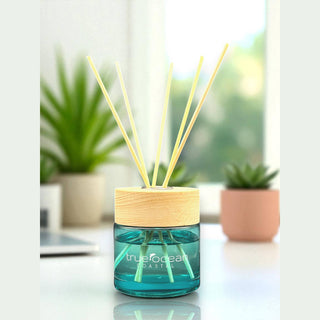 Blue diffuser with wooden cap on a white surface with plants in the background
