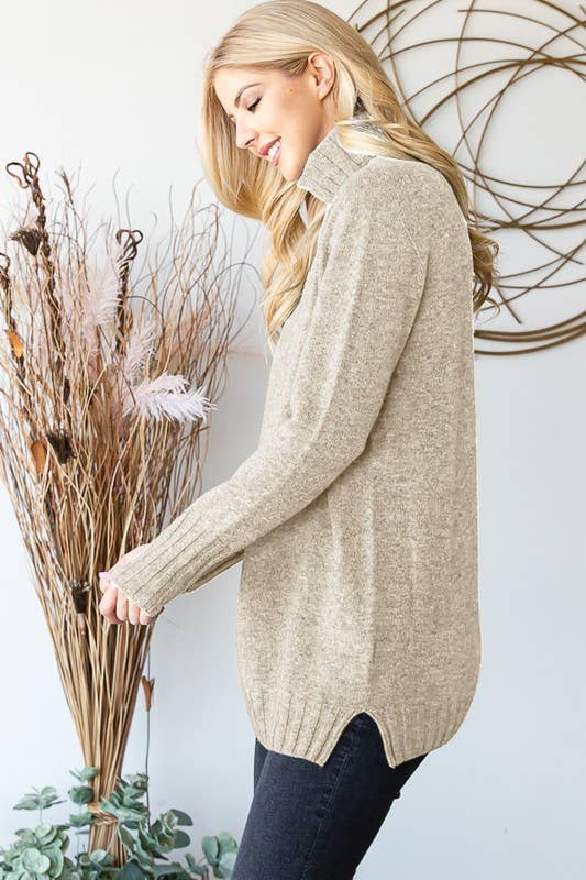 Woman wearing a beige sweater holding dried plants against a white wall.
