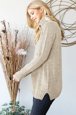 Woman wearing a beige sweater holding dried plants against a white wall.