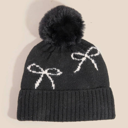Dark gray knit beanie with white bows and black pom-pom on a beige background