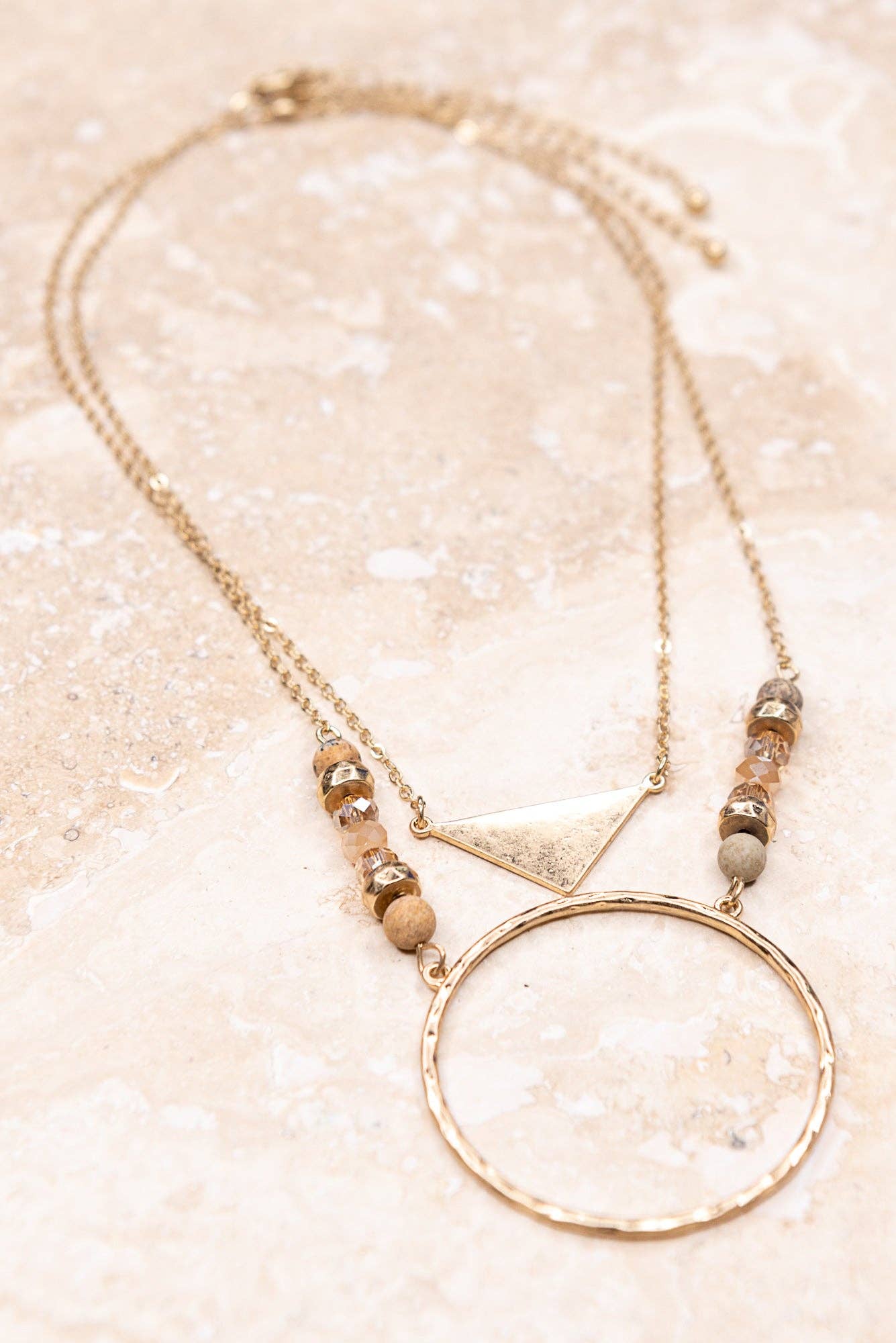 Necklace with geometric pendant and beads on a glittery beige background