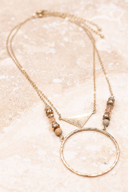 Necklace with geometric pendant and beads on a glittery beige background
