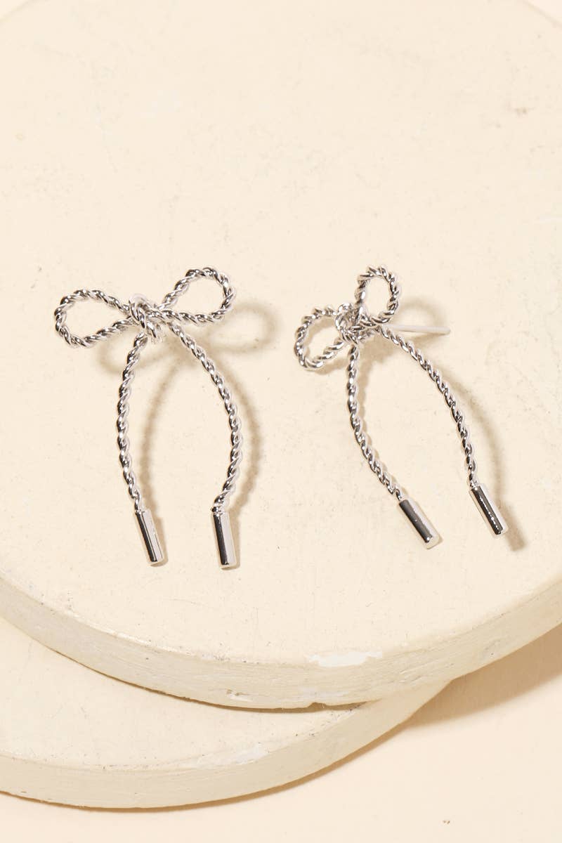 Pair of silver bow-shaped earrings on a beige background
