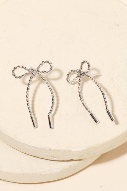 Pair of silver bow-shaped earrings on a beige background