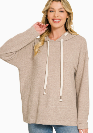 A woman wearing a light beige oversized pullover hoodie with cream-colored drawstrings, paired with blue jeans, against a plain white background.