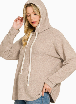 A woman wearing a light beige oversized pullover hoodie with cream-colored drawstrings, paired with blue jeans, against a plain white background.