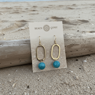 Close-up of Mila Earrings Blue Sky Gold dangle earrings laid flat, showing their gold detail