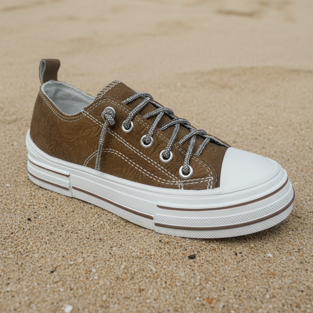 A low-top canvas sneaker in brown with a textured finish, featuring a white rubber toe cap and a thick white sole with a thin brown stripe.