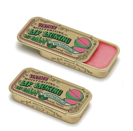 A vintage-style gold metal tin with a green and pink label that reads 'Lip Licking Lip Balm'. The tin is open revealing a clear lip balm inside.